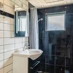 Badezimmer mit Dusche, Waschbecken und Spiegel. Schwarze Fliesen und Holzelemente.