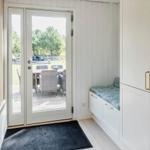 Eingangsbereich mit Glastür, Holzwand und weißen Schränken mit Sitzbank.