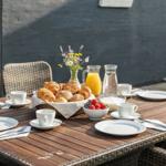 Außenbereich mit gedecktem Tisch, Körben mit Brötchen, Obst und Getränken.