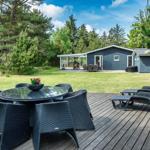 Terrasse mit Tisch, Stühlen und Liegen. Im Hintergrund Haus mit Garten und Spielplatz.