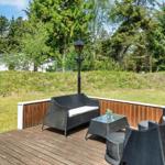 Terrasse mit Sitzgruppe, Tisch und Lampen. Hintergrund: Grasfläche und Bäume.