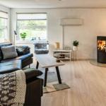 Wohnzimmer mit Sofa, Kamin und TV. Holzboden und große Fenster.