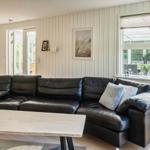 Wohnzimmer mit schwarzer Ledercouch, Holzboden und großem Fenster zur Terrasse.