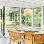 Terrassensitzgruppe mit Glasrundtisch und Rattanstühlen. Durchgehende Glaswände blicken auf Garten und Pool.
