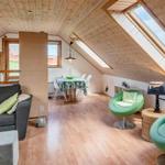 Dachgeschosswohnung mit Holzdecke, grünen Sesseln und Essbereich.