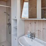 Bad mit Dusche, Waschbecken und Spiegelschrank. Holzwand und Duschvorhang mit Streifen.
