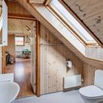 Badezimmer mit Toilette und Waschbecken unter Dachschräge mit Holzwandverkleidung und Dachfenster.