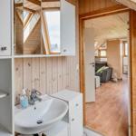 Badezimmer mit Waschbecken und Spiegelschrank. Durchgang in Wohnbereich mit Holzdecke.