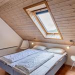 Schlafzimmer mit Dachschrägen, Dachfenster und zwei weißen Stühlen.