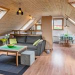 Dachgeschosswohnung mit Sofa, Esstisch und grünen Sesseln. Holzdecke und große Dachfenster.