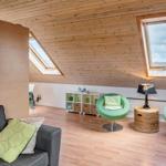 Wohnraum mit Holzdecke, grünen Sesseln und Dachfenstern.
