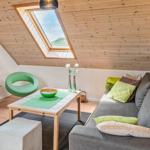 Wohnzimmer mit Sofa, grüner Sessel und Dachfenster. Holzdecke und Fernseher sichtbar.