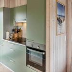 Küche mit grünen Schränken, Herd und Backofen. Holzwände und Tür zum Balkon.