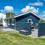 Ein dunkelblauer Ferienhaus mit Terrasse und Garten. Ein Gartenmöbel und Grill sind vorhanden.