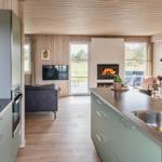 Küche mit Arbeitsplatte und Spüle. Im Hintergrund Wohnbereich mit Kamin und Fernseher.