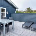 Terrasse mit Tisch, Stühlen und Liegen. Dunkelblaue Wand und Holzdielen.