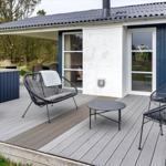 Terrasse mit drei Stühlen und Tisch vor blauem Haus mit Glasfenstern.