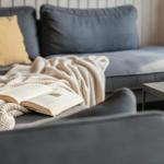 Ein grauer Sofa mit Kissen und einer Decke. Ein Buch liegt darauf.
