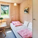 Schlafzimmer mit Holzwand, Bett, Tisch und Fenster zur grünen Umgebung.