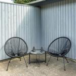 Terrasse mit zwei schwarzen Sesseln, Tisch und Pflanzen an grauer Holzwand.