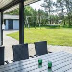 Terrasse mit Tisch und Stühlen, Blick auf grünen Garten mit Schaukel und Trampolin.