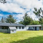 Ein graues Haus mit Dach und Garten. Umgeben von Bäumen und Gras.