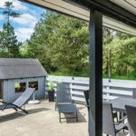 Terrasse mit Tisch, Stühlen und Liegestühlen. Im Hintergrund ein kleines Holzhaus und Wald.
