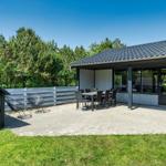 Haus mit Terrasse, Tisch, Stühlen und Grillhütte im Grünen.