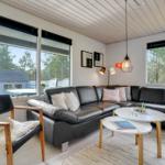 Wohnzimmer mit schwarzer Ledercouch, Holzstuhl und großen Fenstern.