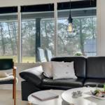 Wohnzimmer mit schwarzer Ledercouch, runden Tisch und Blick auf Wald.
