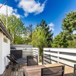 Terrasse mit Tisch, Stühlen und Liegestühlen. Hintergrund: Bäume und blauer Himmel.