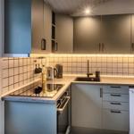 Küche mit Arbeitsplatte, Spüle und Kühlgerät. Hintergrund mit Fliesen und Licht.