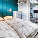 Schlafzimmer mit Bett, blauer Wand und Blick in Wohnbereich mit TV.