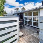 Terrasse mit Sitzgelegenheit und Glasfront zum Haus. Holzgeländer und grüne Umgebung.