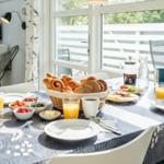 Frühstückstablett mit Brot, Obst und Getränken vor großem Fenster.