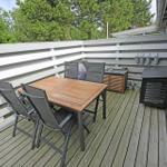 Terrasse mit Holztisch, Stühlen und Grillplatz. Umzäunt mit weißem Holzgeländer.