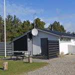 Ein Haus mit Grillplatz, Satellitenschüssel und Holzverkleidung. Gras, Kies und Bäume umgeben es.