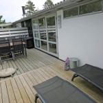 Terrasse mit Tisch, Stühlen und Liegen. Hintergrund: Haus mit Glasfront und Bäumen.