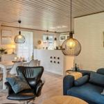 Wohn- und Essbereich mit Sofa, Sessel und Tisch. Decke aus Holz, weiße Wände und Beleuchtung.
