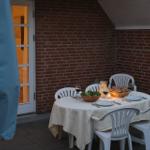 Rundtisch mit Tischdecke, Tellern und Stühlen auf Terrasse mit Backsteinwand.
