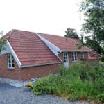 Ein Haus mit rotem Dach und Backsteinfassade umgeben von Grünflächen und Bäumen.
