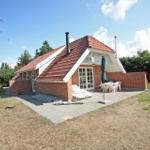 Haus mit Terrasse, Liegen und Tisch. Umgeben von Grün und Bäumen.