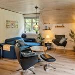 Wohnzimmer mit blauem Sofa, schwarzen Sesseln und Holzboden. Fenster, Pflanzen und Beleuchtung sichtbar.