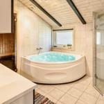 Badezimmer mit Whirlpool, Dusche und Waschbecken. Holzdecke und Fliesenwand.