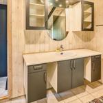 Badezimmer mit Waschbecken, Spiegelschrank und Dusche. Holzwände und Fliesenboden.