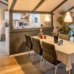 Essbereich mit Tisch und Stühlen, Küchenbereich im Hintergrund, Holzwände und Pflanzen.