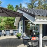 Terrasse mit Sonnenschirm, Tisch und Stühlen vor einem Haus mit blauem Holzverkleidung.
