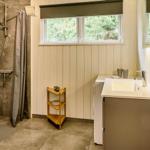 Badezimmer mit Dusche, Waschbecken und Fenster mit Blick auf Bäume.