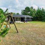 Schwarzes Haus mit Terrasse und Spielplatz im Grünen.