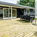 Holzterrasse mit Sitzgruppe und Blick ins Haus. Garten mit Pflanzen und Bäumen.